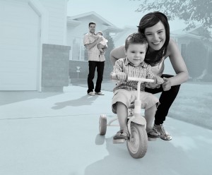 Portrait of pretty cheerful mother teaching her son to ride tricycle
